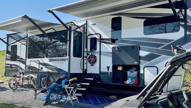 Class A Motorhome, with RV awning extended in RV Park with sun setting.