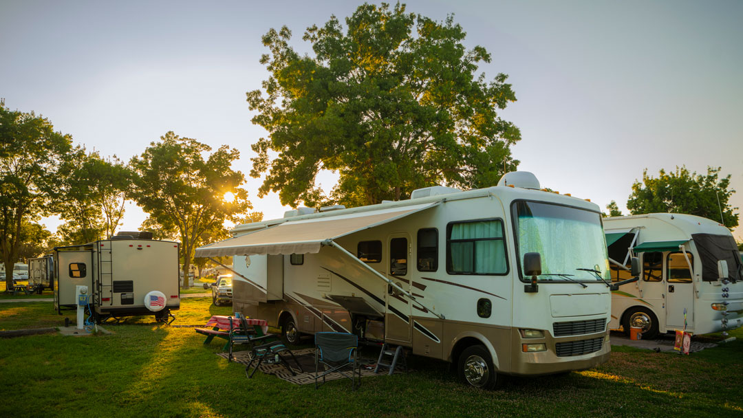 Class A Motorhome, with RV awning extended in RV Park with sun setting.